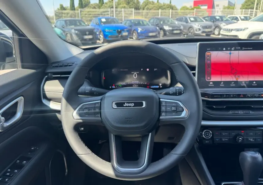 Vue intérieure centrée sur le volant Jeep d'un Compass blanc 2025, avec tableau de bord numérique et écran tactile large.