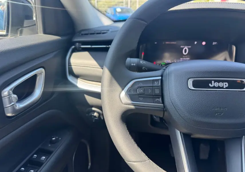 Vue rapprochée du volant et tableau de bord du Jeep Compass blanc, avec commandes au volant et affichage numérique.