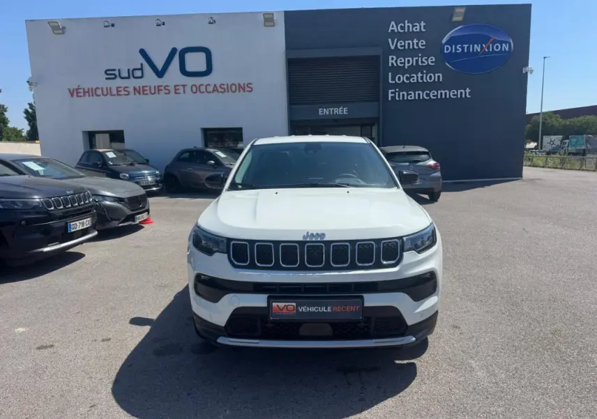 Jeep Compass blanc vue de face, calandre distinctive à sept fentes, stationné devant un bâtiment commercial.