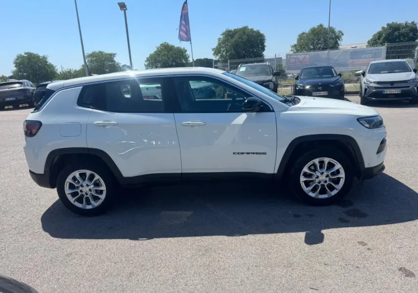 Vue de profil côté gauche d'un Jeep Compass blanc 2025 avec jantes alliage et logo "Compass" visible sur la porte.