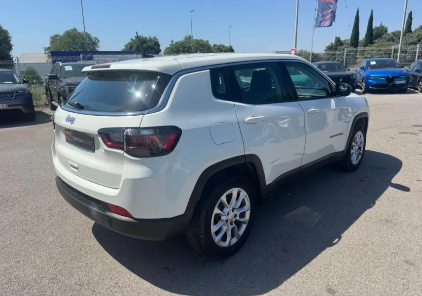Jeep Compass blanc vue 3/4 arrière droit, avec jantes alliage et feux arrière LED visibles en plein jour.