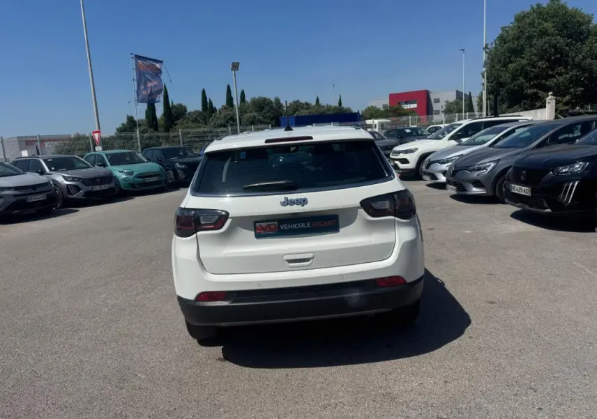 Vue arrière d'un Jeep Compass blanc 2025 garé en extérieur, avec feux arrière LED et logo Jeep bien visible.
