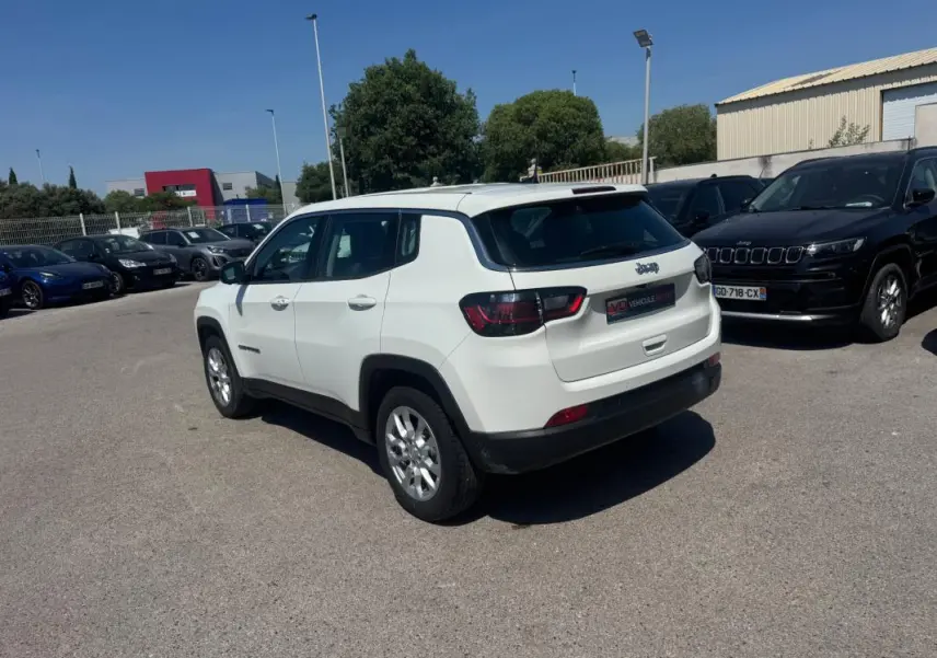 Vue 3/4 arrière droite d'un Jeep Compass blanc stationné en extérieur sous un ciel dégagé.