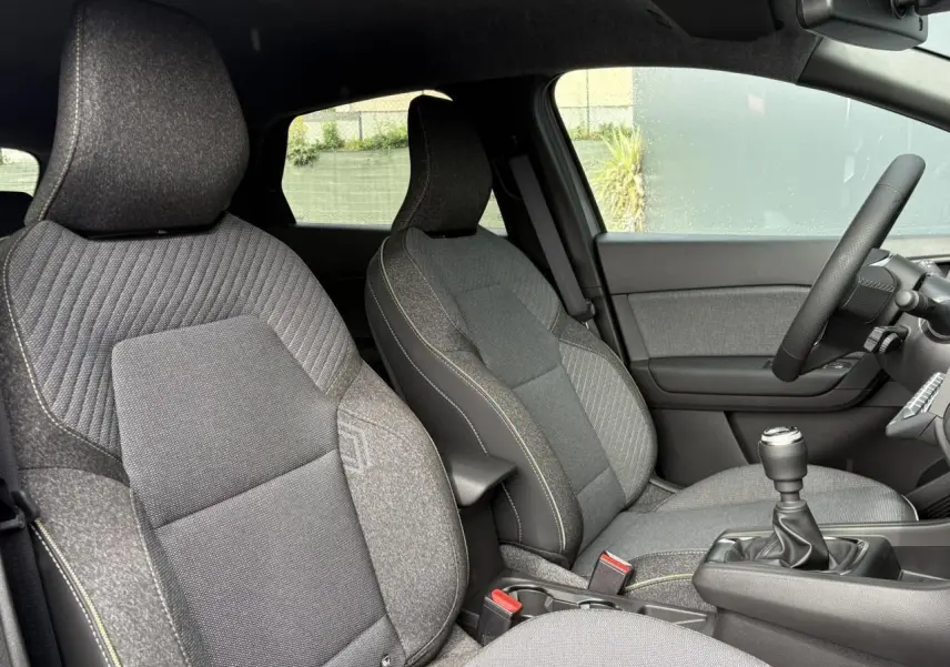 Vue intérieure côté conducteur du Renault Captur 2025, sièges gris avec coutures contrastées et levier de vitesse manuel.