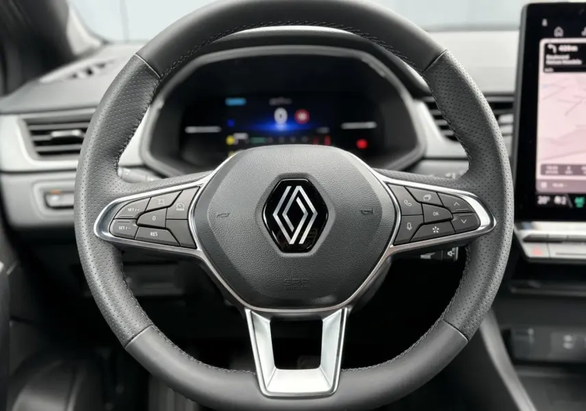 Vue rapprochée du volant cuir perforé du Renault Captur 2025 avec commandes intégrées et tableau de bord numérique flou.