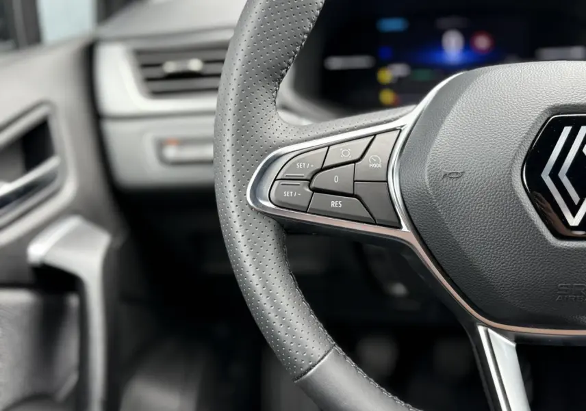 Gros plan sur le volant en cuir perforé du Renault Captur 2025 avec commandes intégrées et tableau de bord flou.