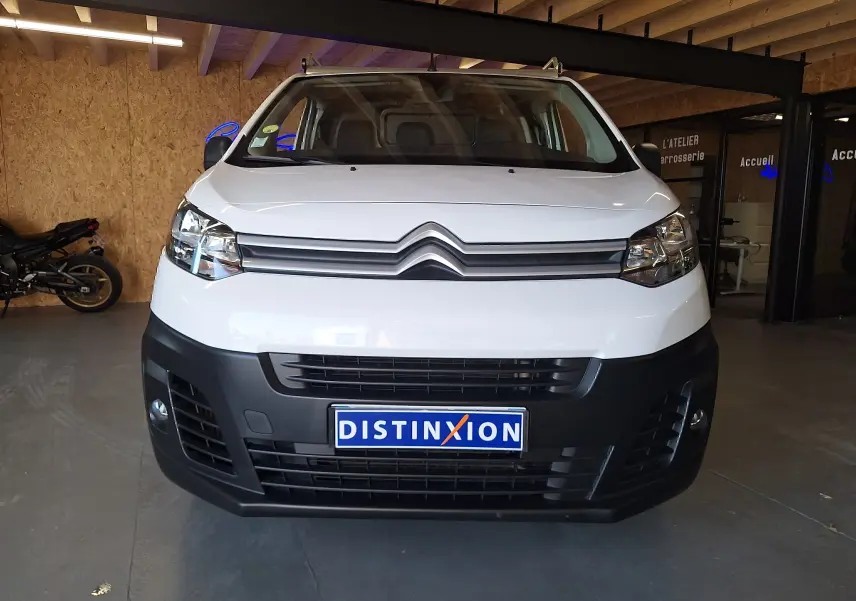 Vue frontale d'un Citroën Jumpy blanc 2020 avec calandre noire et plaque Distinxion en intérieur d'atelier.
