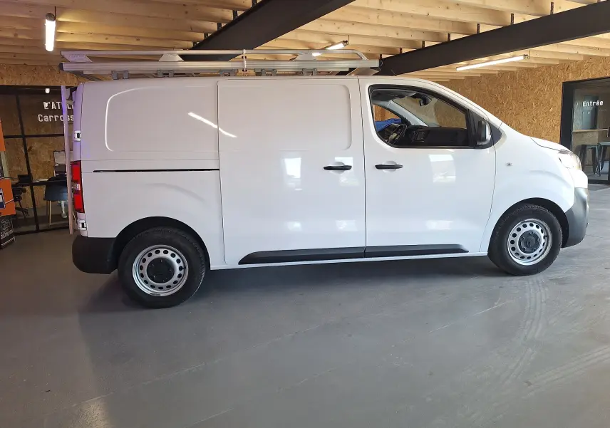 Profil côté droit d’un utilitaire blanc Citroën Jumpy 2.0 BlueHDi 120 Club 2020 avec galerie de toit en intérieur.