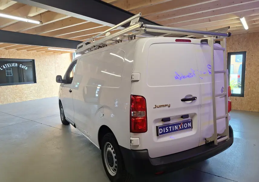 Vue 3/4 arrière droite du Citroën Jumpy blanc 2020 avec galerie et échelle métallique dans un garage.