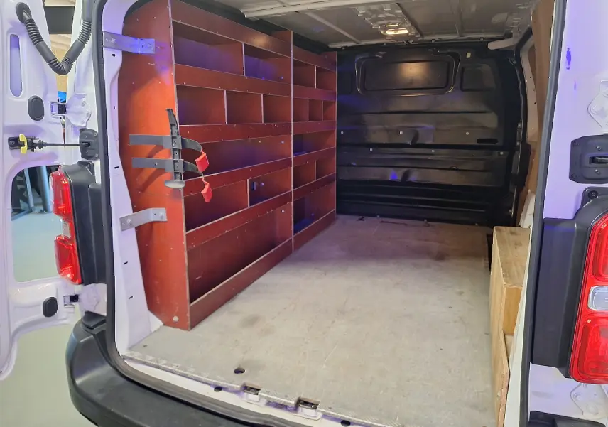 Intérieur arrière du Citroën Jumpy blanc 2020, montrant les portes ouvertes et des étagères en bois sur le côté gauche.