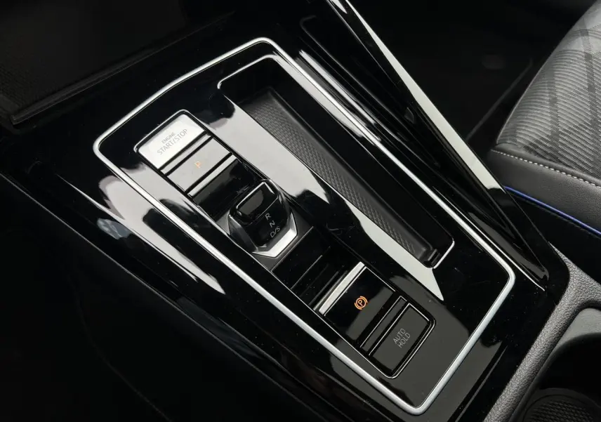 Vue rapprochée de la console centrale noire brillante de la Volkswagen Golf VIII avec sélecteur de vitesse DSG et boutons Start/Stop et frein électrique.