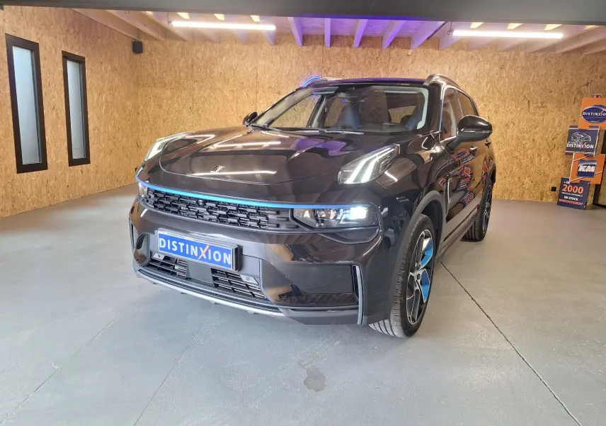 Vue 3/4 avant du SUV LYNK & CO 01 noir avec détails bleus sur la calandre et jantes dans un garage éclairé.