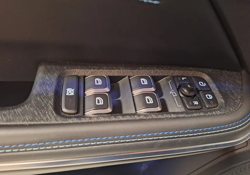 Gros plan sur les commandes des vitres et rétroviseurs côté gauche d’un LYNK & CO 01 noir avec surpiqûres bleues.