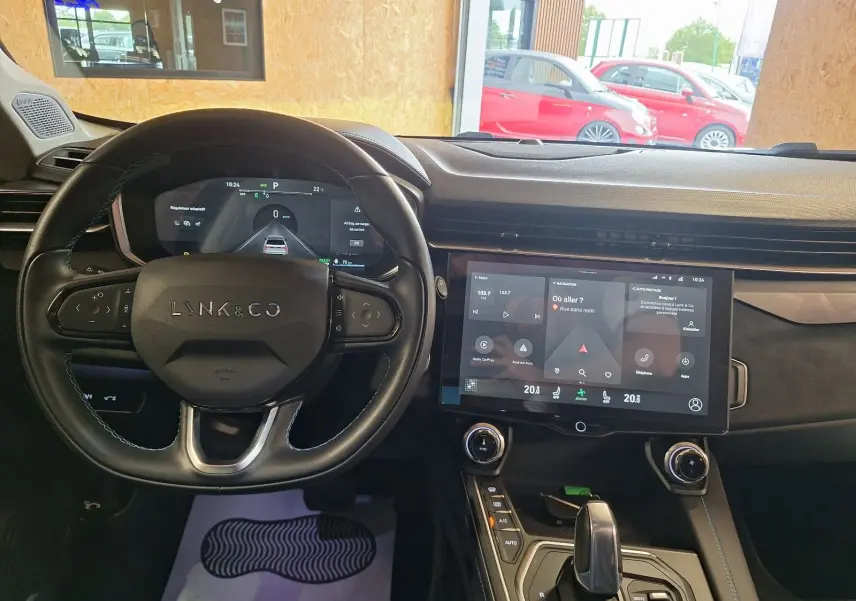 Vue intérieure du tableau de bord et volant noir du Lynk & Co 01 hybride rechargeable 2023 avec écran tactile central allumé.