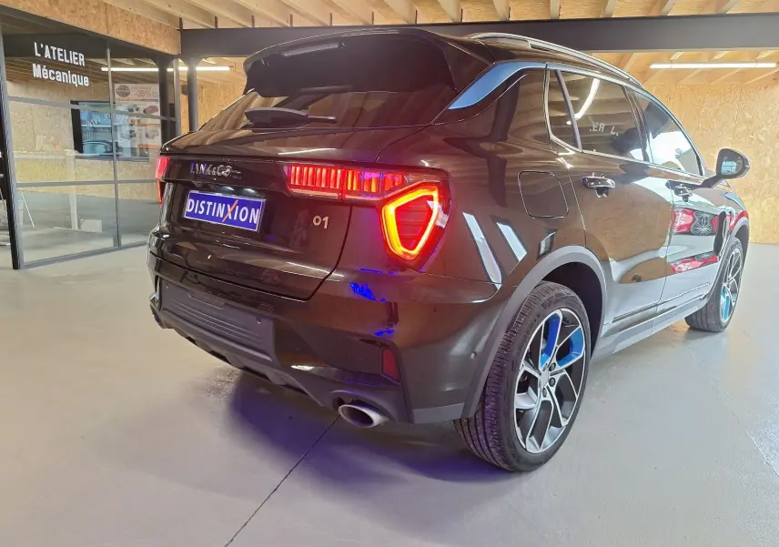 Vue 3/4 arrière droite d'un SUV LYNK & CO 01 noir avec feux arrière allumés et jantes bicolores en intérieur d'atelier.