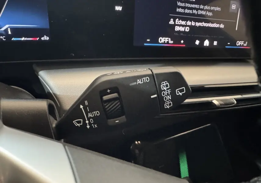 Gros plan sur la commande d’essuie-glace à gauche du volant du BMW X1 gris foncé 2024 avec affichage digital en arrière-plan.