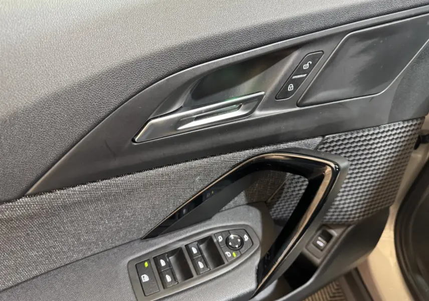 Gros plan sur la porte côté conducteur de la BMW X1 2024 gris foncé, avec commandes de vitres et verrouillage.