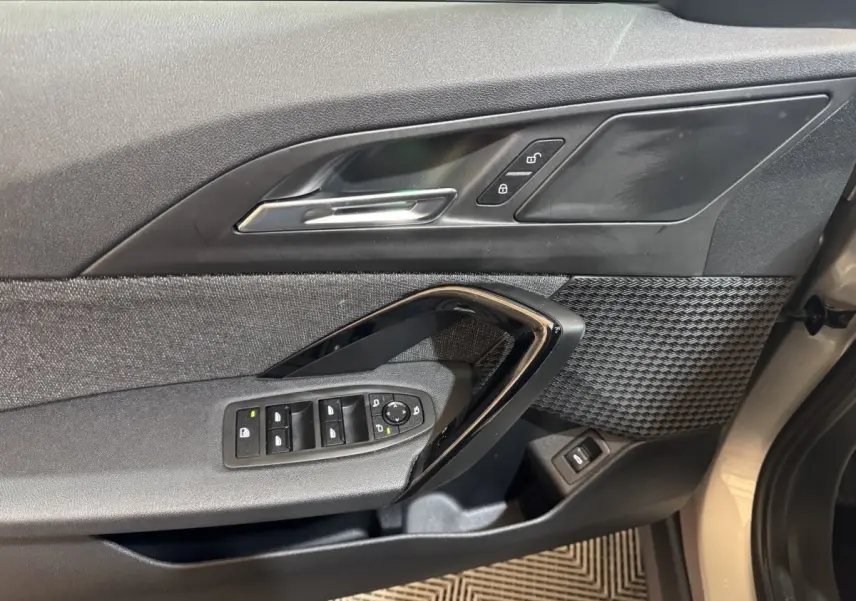 Vue rapprochée de la porte avant gauche gris foncé de la BMW X1 avec commandes électriques et insert décoratif texturé.