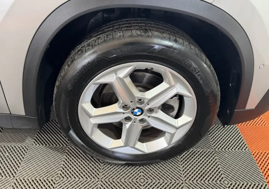 Gros plan sur la roue avant droite d’un BMW X1 gris foncé, avec jante alliage et passage de roue noir.