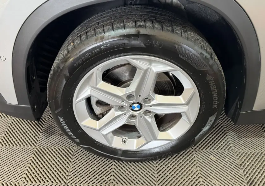 Gros plan sur la roue avant droite avec jante argentée et logo BMW, partie de la carrosserie gris foncé visible.