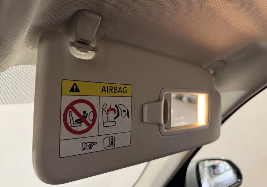 Détail du pare-soleil côté conducteur beige avec miroir éclairé et avertissement airbag, rétroviseur extérieur visible.