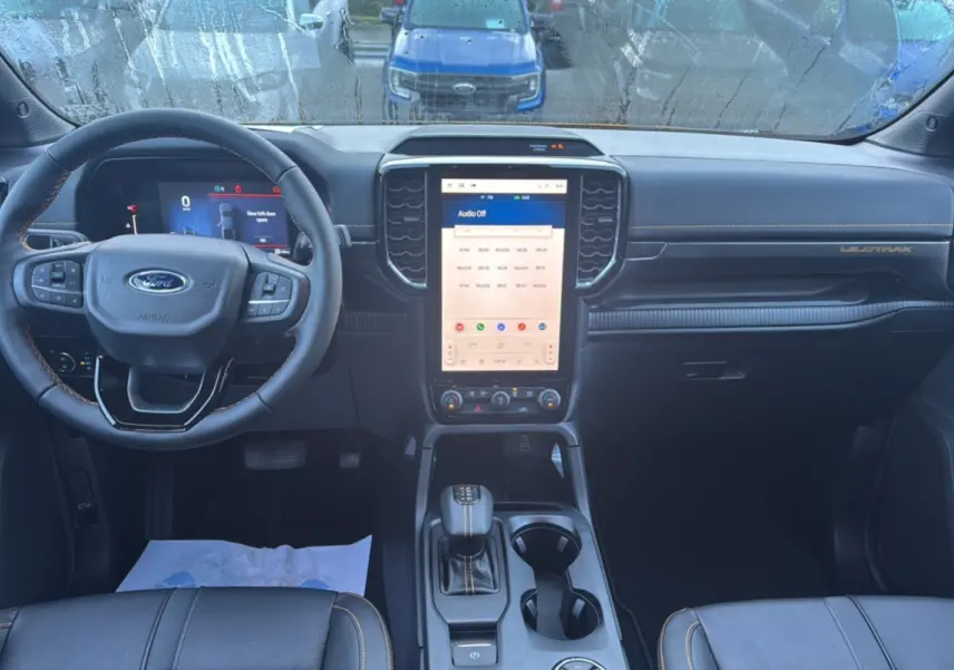 Vue intérieure avant du Ford Ranger Wildtrak 2026, tableau de bord noir avec écran tactile vertical et volant cuir multifonctions.
