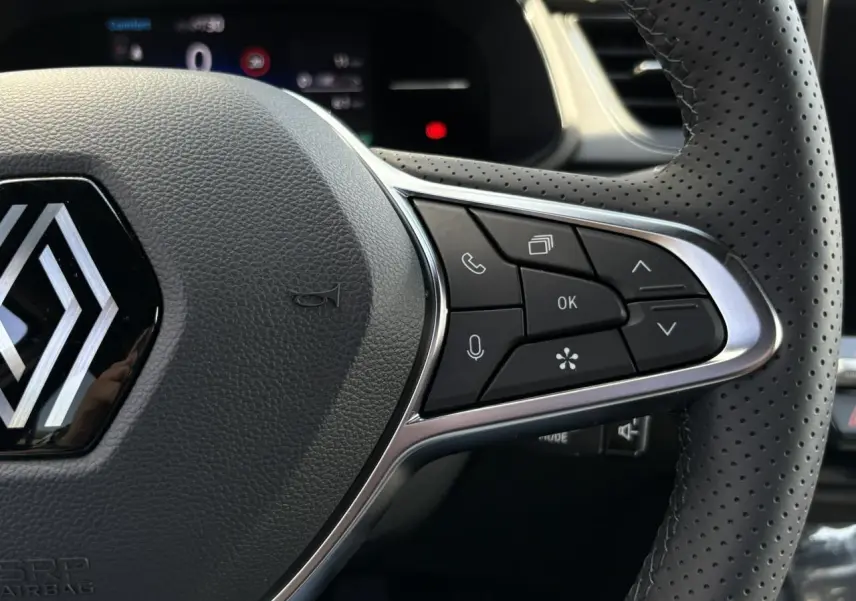 Gros plan sur le volant perforé noir du Renault Captur 2025 avec commandes multifonctions et logo central chromé.