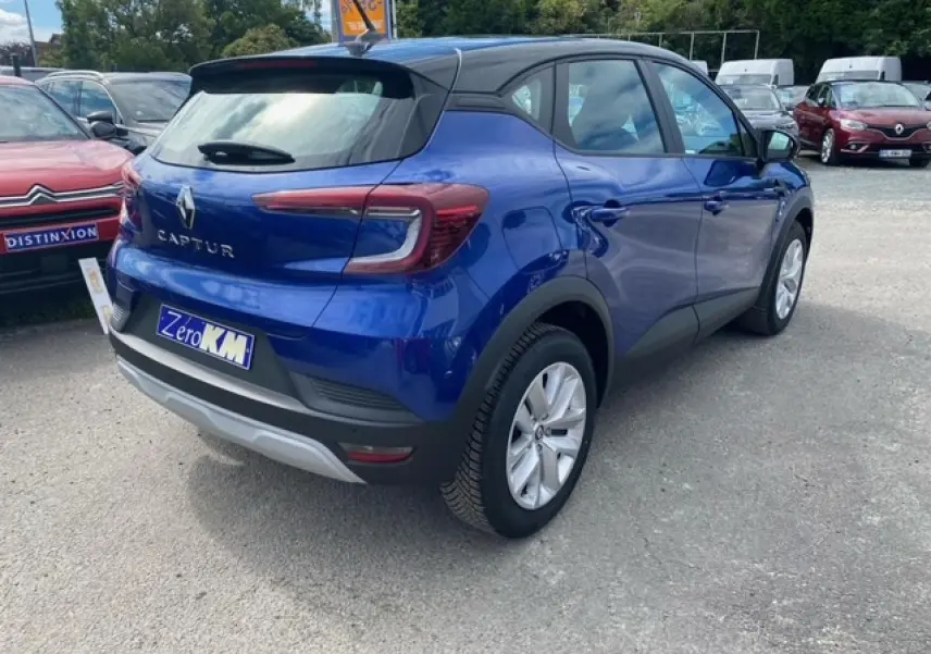 Vue 3/4 arrière droite d'un Renault Captur bleu Iron 2023 avec toit noir et jantes argentées sur parking.