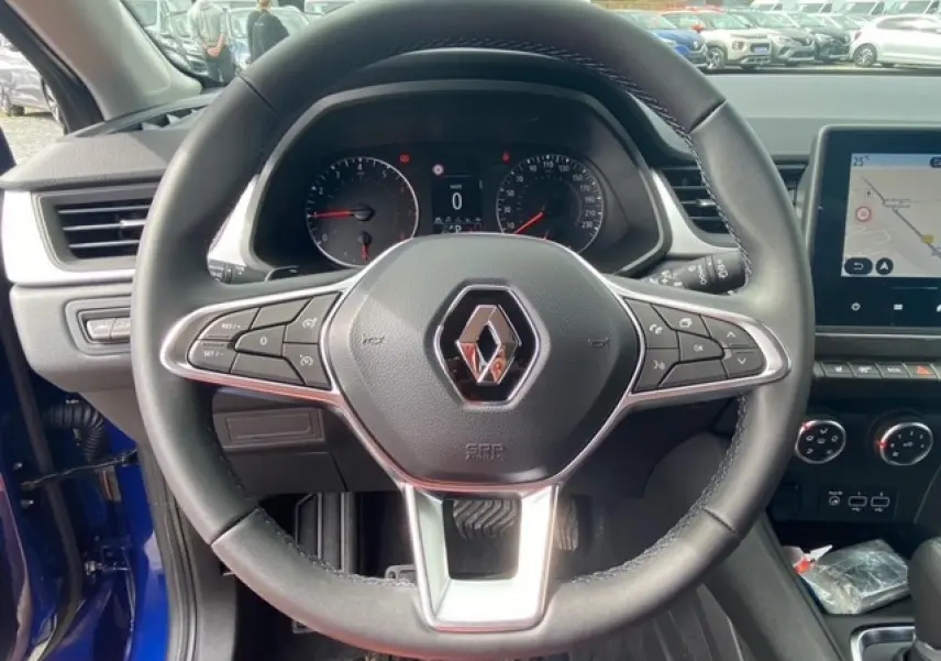 Vue intérieure centrée sur le volant du Renault Captur bleu 2023 avec tableau de bord et écran de navigation visible.