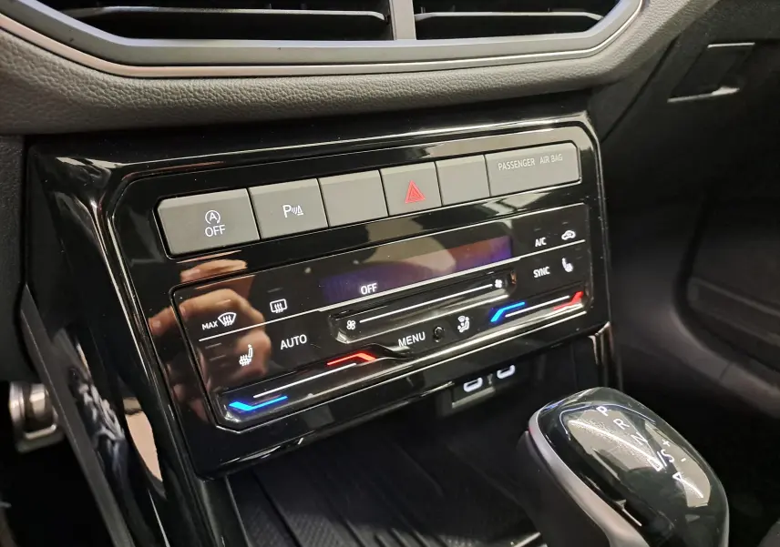 Gros plan sur la console centrale noire brillante du Volkswagen T-Cross 2025 avec commandes climatisation et levier de boîte automatique.