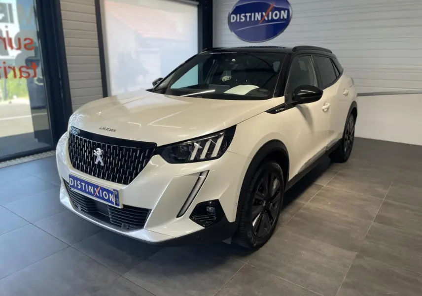 Peugeot 2008 blanc vue 3/4 avant droit en intérieur avec calandre noire et jantes foncées.