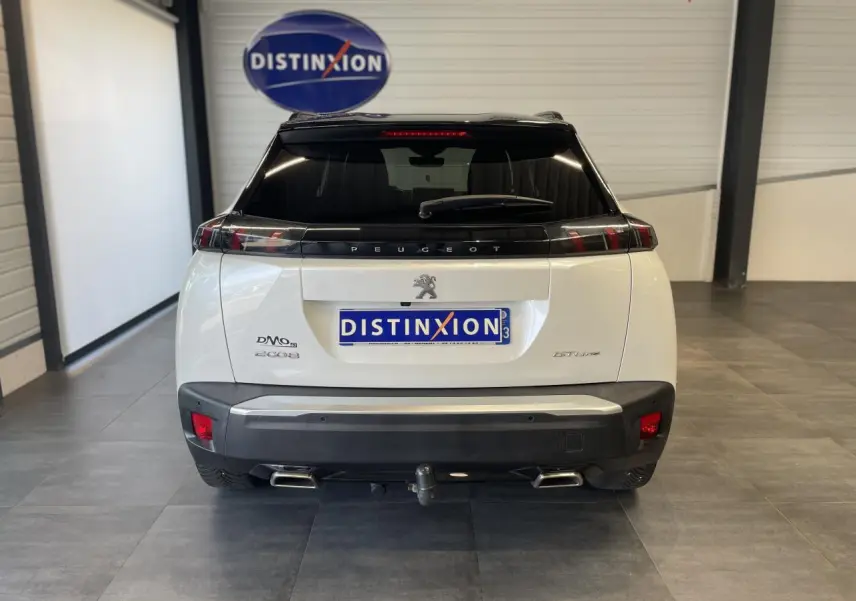 Vue arrière d'un Peugeot 2008 blanc avec toit noir, double sortie d'échappement chromée et attelage visible.