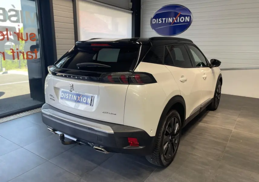 Vue 3/4 arrière droite du Peugeot 2008 GT Line blanc avec toit noir et attelage en intérieur showroom.