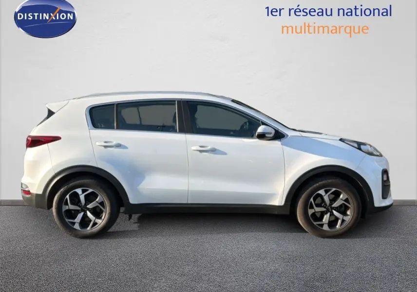 Vue de profil côté gauche d’un KIA Sportage blanc nacré 2021 avec jantes alliage bicolores et carrosserie compacte.