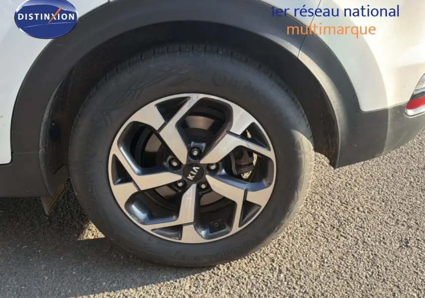 Gros plan sur la roue arrière droite d’un Kia Sportage blanc nacré avec jante alliage 5 branches bicolore.