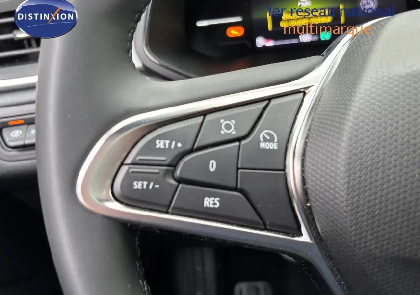 Gros plan sur les commandes de régulateur de vitesse au volant d’un Renault Symbioz blanc nacré, tableau de bord numérique en arrière-plan.