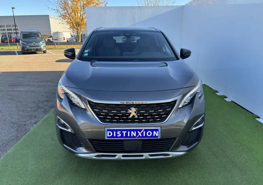Vue avant d'un Peugeot 3008 gris métal de 2020 avec calandre noire et logo lion distinctif sur fond urbain.