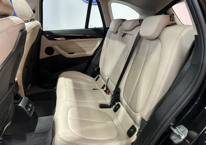 Vue intérieure côté droit des sièges arrière en cuir beige d’un BMW X1 noir, avec ceinture de sécurité et porte ouverte.