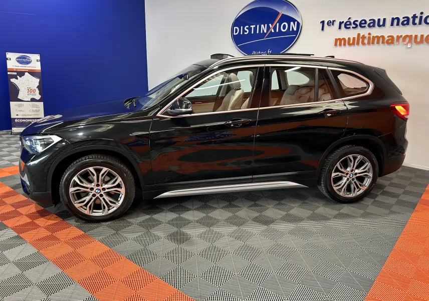 BMW X1 sDrive18iA noir vue de profil côté gauche en intérieur avec toit ouvrant et barres de toit neuves visibles.
