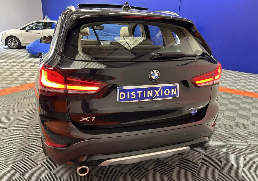 Vue arrière d'un BMW X1 noir avec feux allumés dans un showroom au sol à damier.