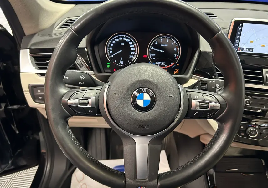 Vue rapprochée du volant cuir noir BMW X1 2019 avec tableau de bord et écran GPS intégré visible.