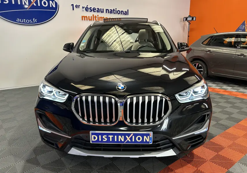 Vue avant d'un BMW X1 noir 2019 avec calandre chromée et phares LED allumés en intérieur showroom.