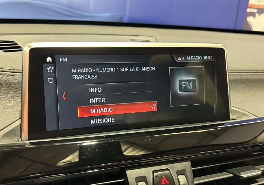 Écran central du tableau de bord BMW X1 affichant la radio FM avec sélection sur M Radio, intérieur noir.