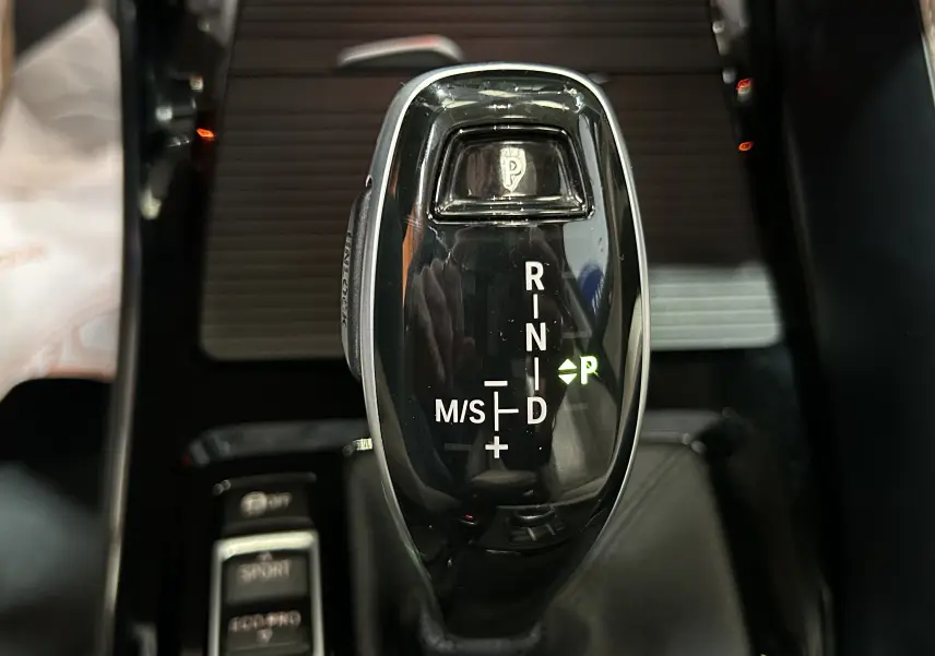Gros plan sur le levier de vitesse automatique noir brillant du BMW X1 sDrive18iA, avec indication mode parking verte.
