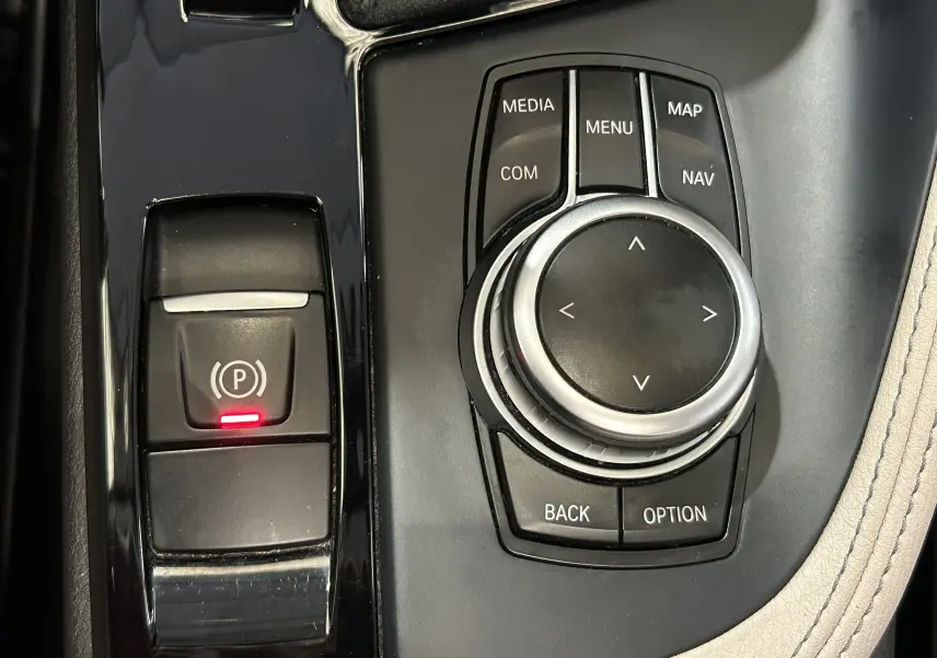 Gros plan sur la molette de commande iDrive et le frein à main électrique avec témoin rouge dans l'habitacle beige du BMW X1 noir.