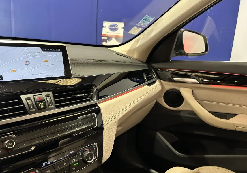 Vue intérieure côté passager du tableau de bord beige et noir avec écran GPS et finitions rouges d'une BMW X1 noire.