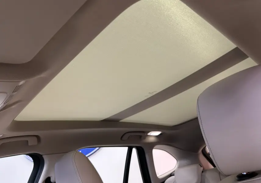 Vue intérieure du toit ouvrant fermé et des sièges avant en cuir clair d’un BMW X1 noir de 2019.