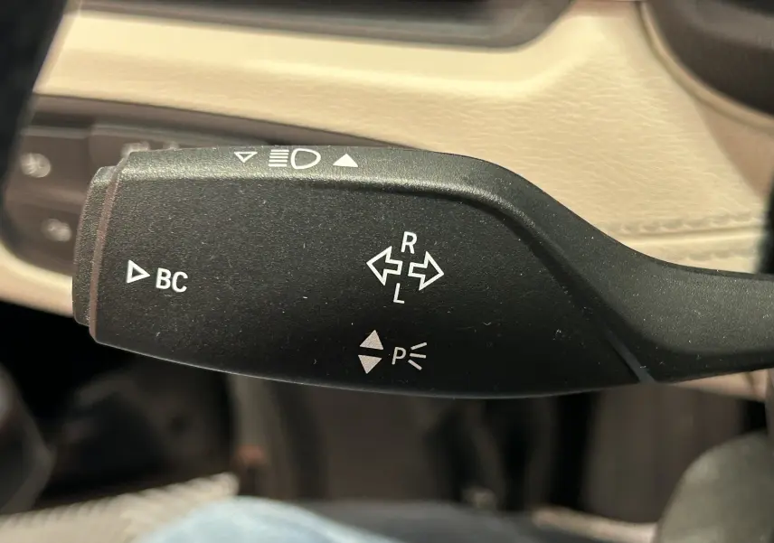 Gros plan sur la manette de clignotant noire à l'intérieur du BMW X1, avec commandes BC et indicateurs lumineux.
