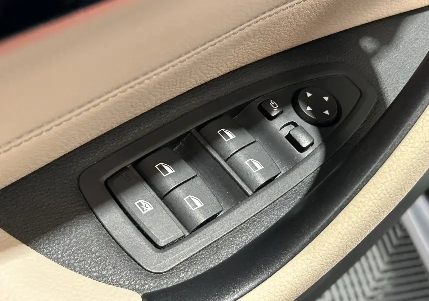 Gros plan sur les commandes des vitres électriques et rétroviseurs sur la porte côté conducteur d’un BMW X1 noir.