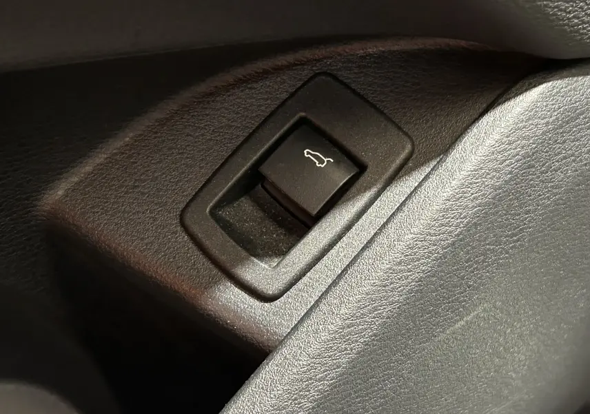 Gros plan sur le bouton d'ouverture électrique du hayon dans l'habitacle d'une BMW X1 noir.